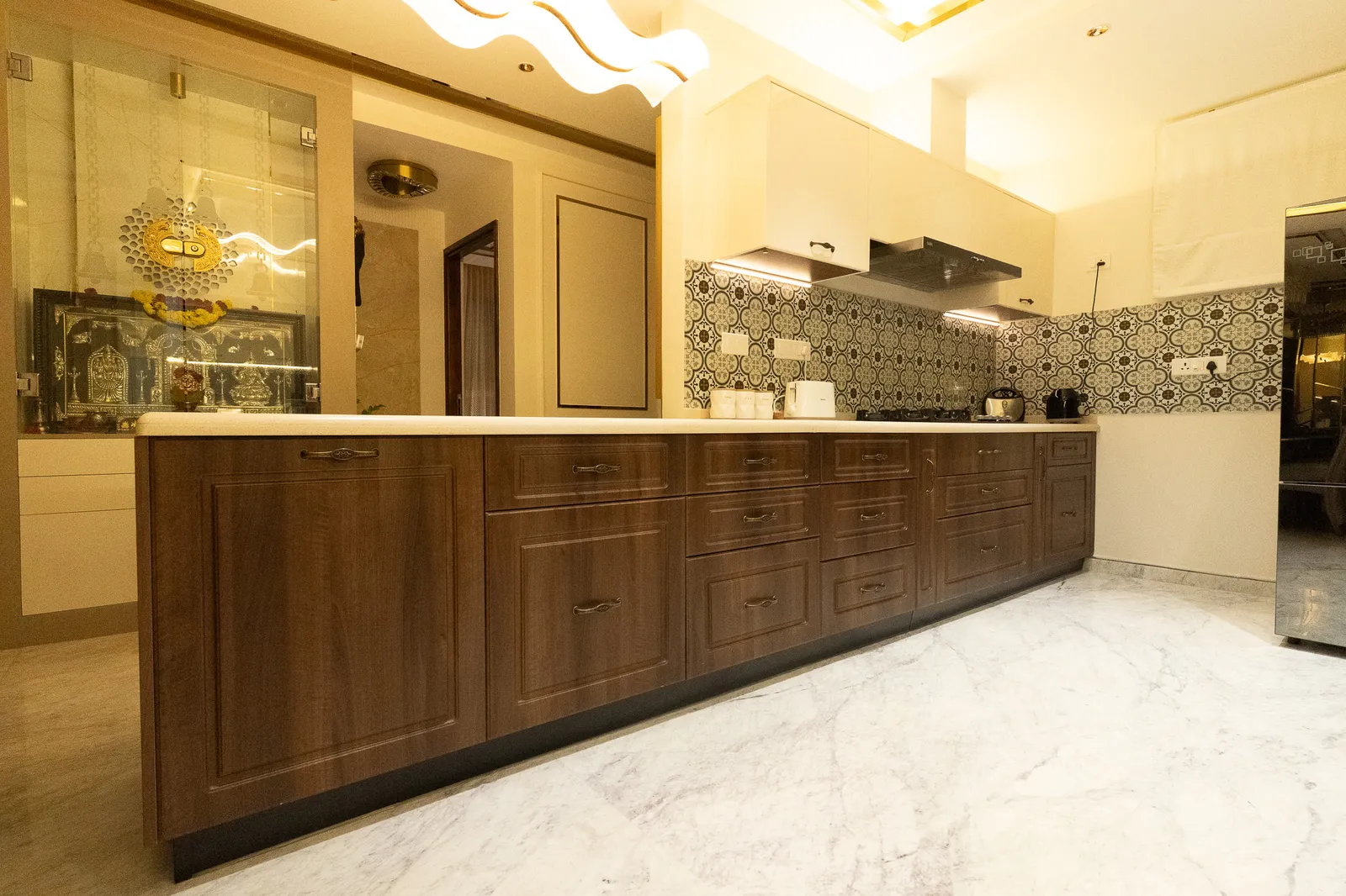 Long walnut kitchen counter with shaker cabinets and patterned tiles — Divyarjuna